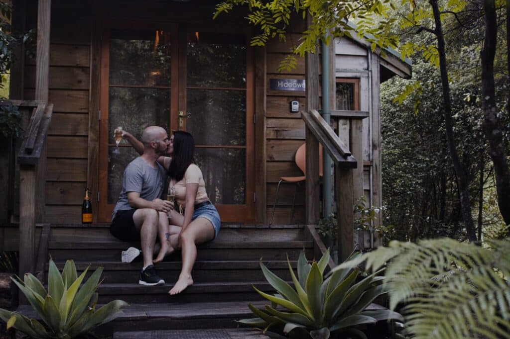 Coromandel Accommodation. Man and woman sitting on the stairs of a wooden cabin at Hush Boutique.