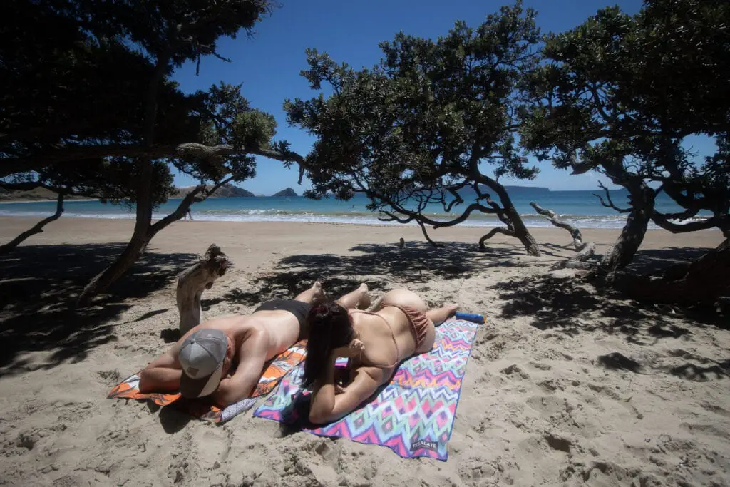 Best Coromandel Beaches. Man and Woman lying on towels at Opito Bay beach