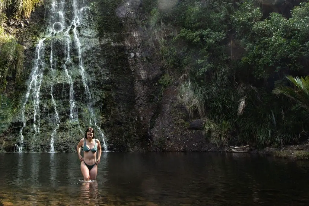 Auckland Waterfalls - Female in a bikini walking through the pool at the bottom of Karekare falls