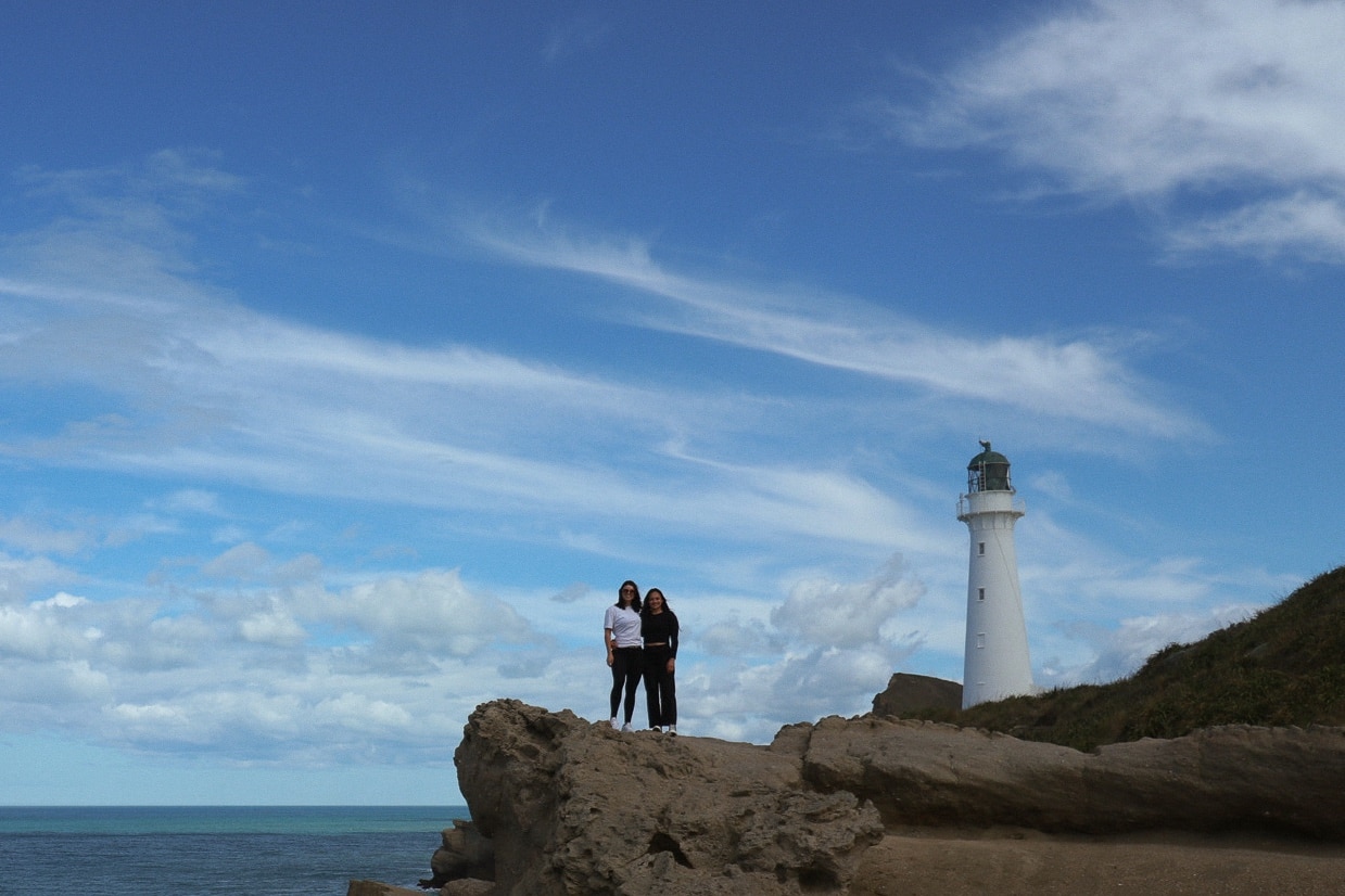 Castle Point Lighthouse is one of the best sunset spots Wellington. The foreground shows two women standing together smiling at the camera, behind them is the tall white castle point lighthouse.