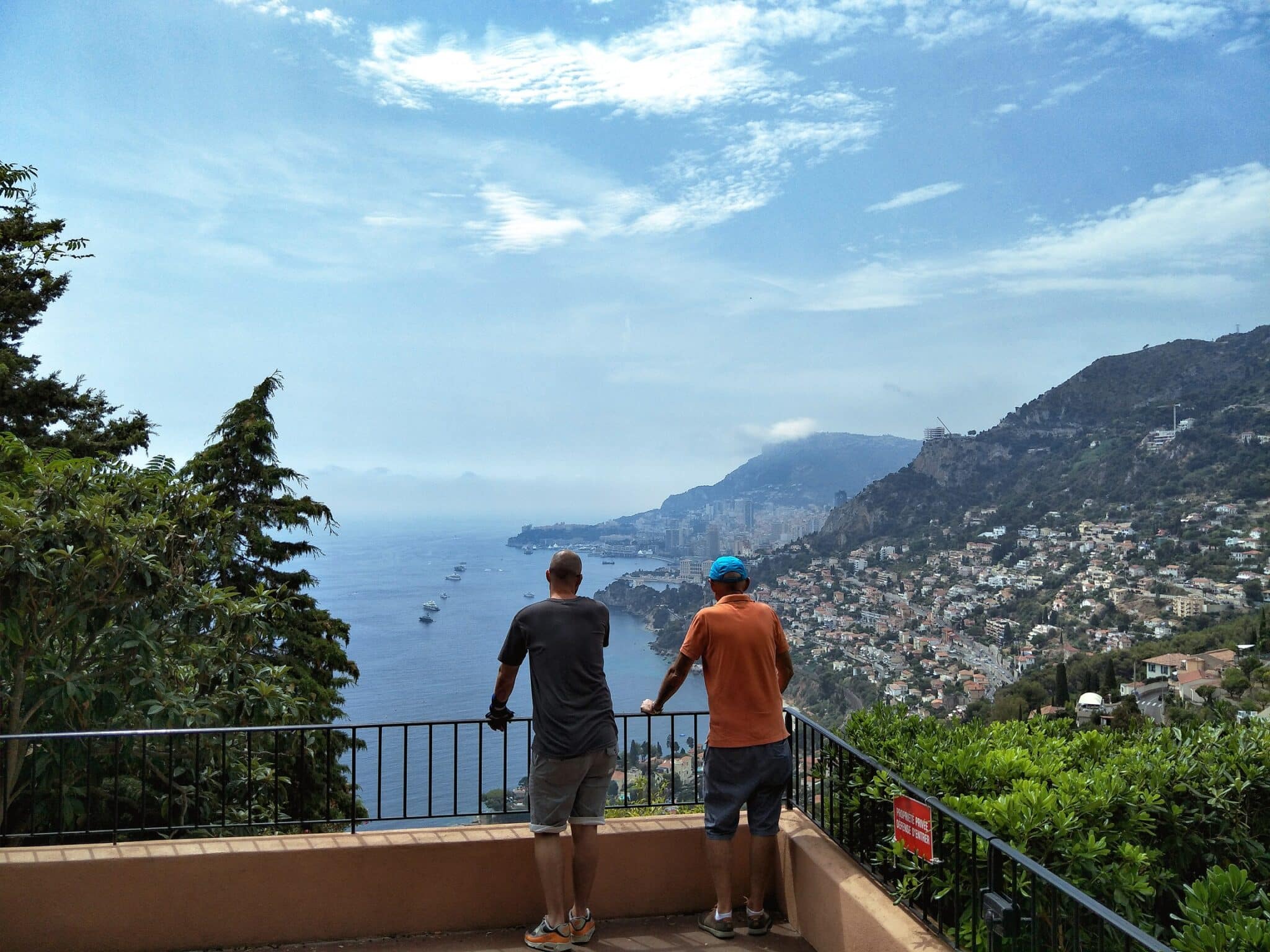 Two men looking over a balcony in Roquebrune France. The view in front of them is over the neighbouring hills covered with houses and small towns.