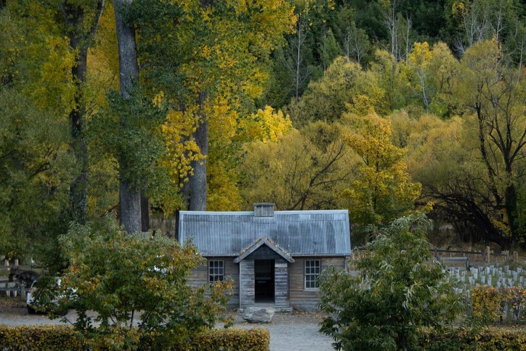 Queenstown Budget Travel Tips: A photo of the Arrowtown cabin. The wooden cabin stands among a canopy of green and gold trees