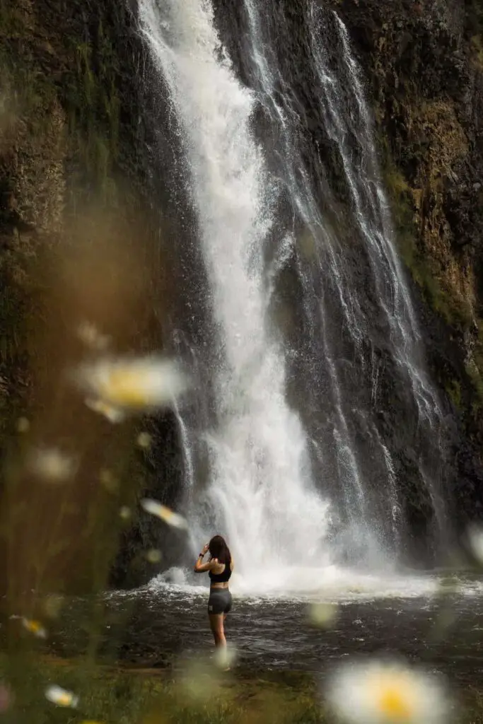 Best waterfalls in Auckland: Female standing next to the gushing waterfall of Hunua Falls