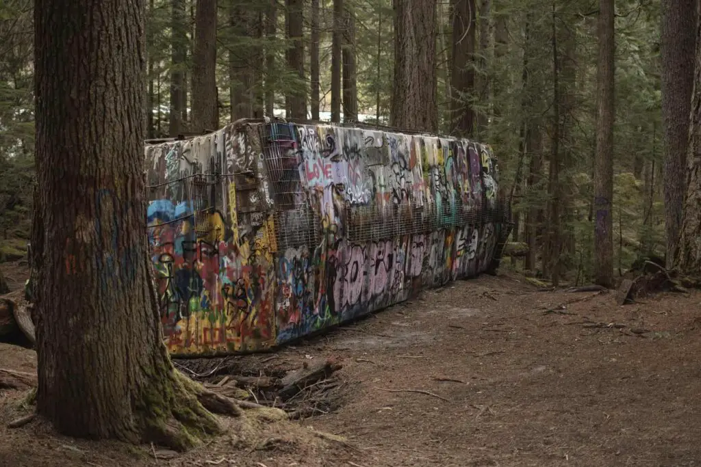 Things to do in Whistler; image of a overturned train carriage covered in spray paint artwork sitting amongst a dense green forest