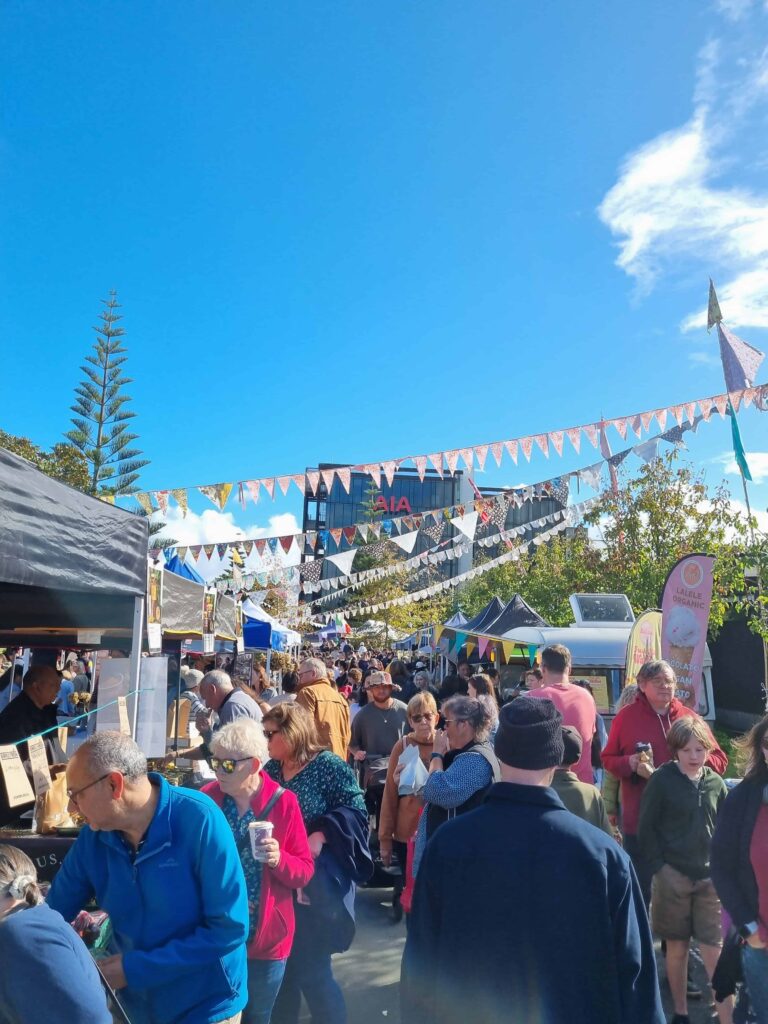 A crowd of people moving between stalls at one of the best Auckland sunday markets at Smales Farm.