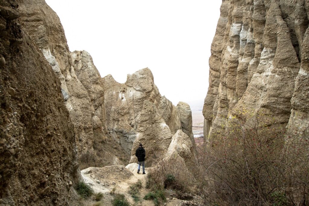 A man standing on the edge of a small rocky ledge in the middle of the Omarama Clay Cliffs