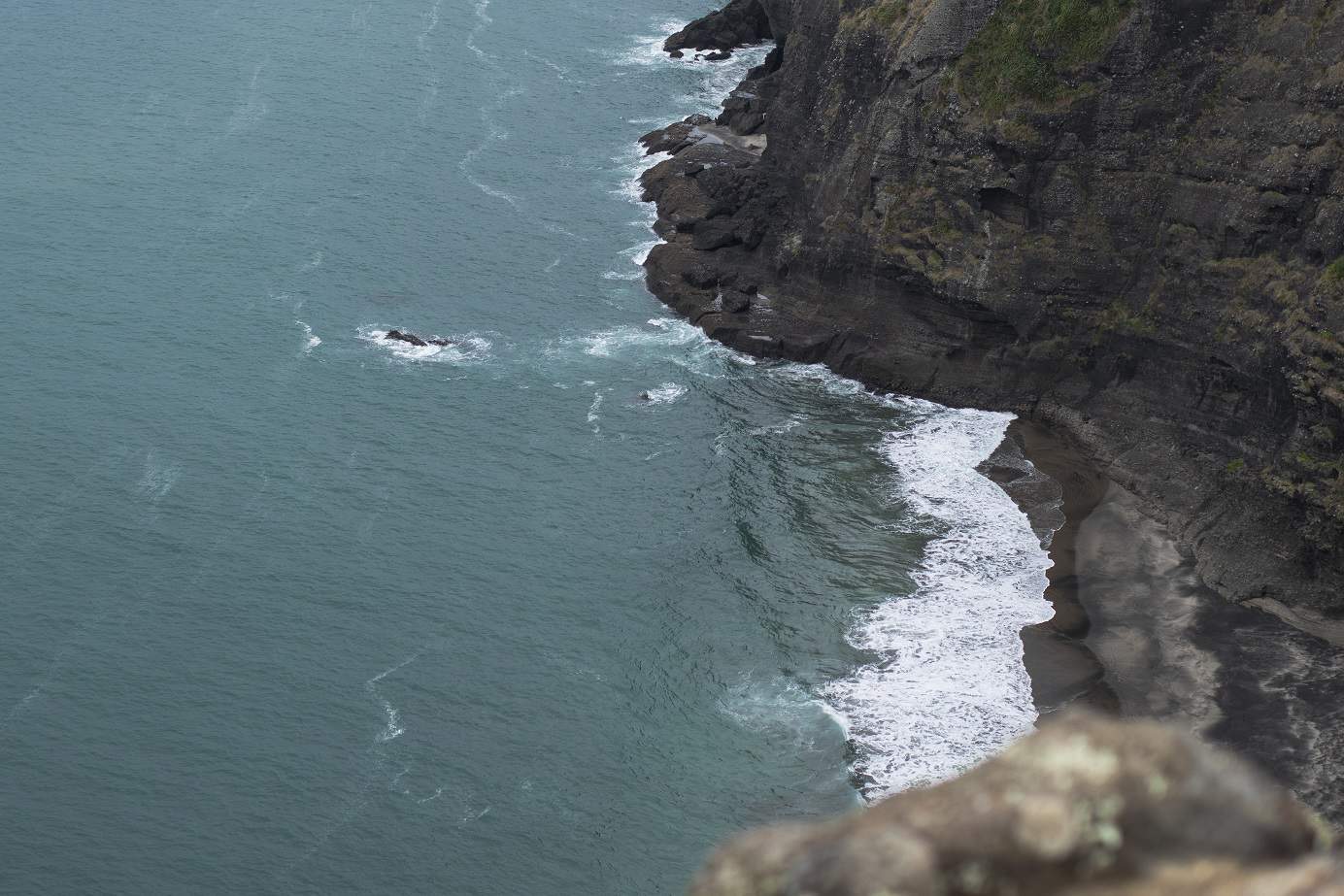 Birds eye view of waves crashing up against cliffs at Mercer Bay Loop bush walk in Auckland
