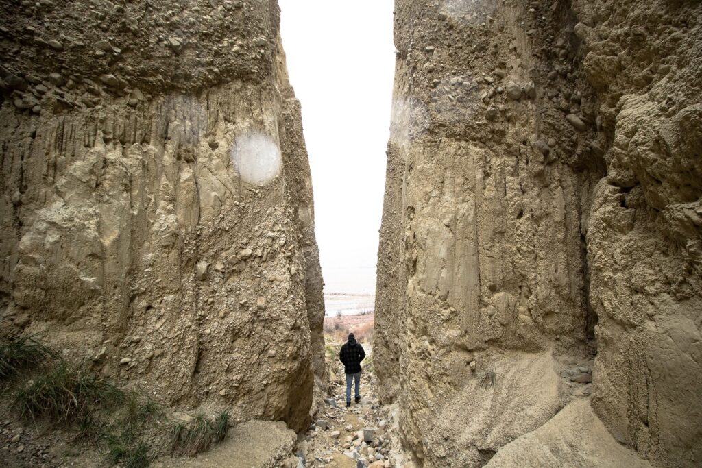 A man standing between two large and close sitting cliffs at Omarama Clay Cliffs