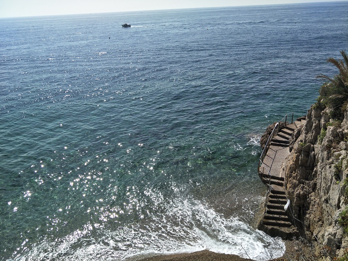 A birds eye view of waves lapping up to a cliff at Monaco beach