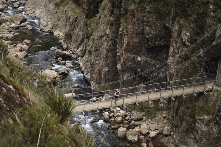 A woman standing on a suspension bridge in the middle of Karangahake Gorge hiking trail