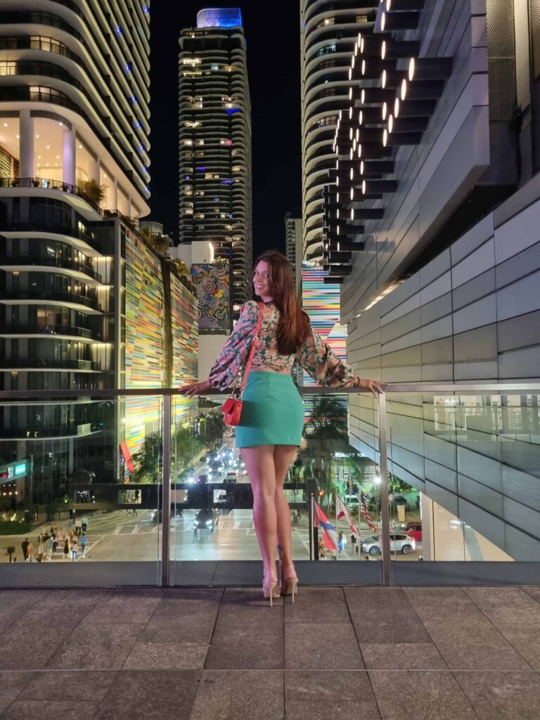 Female standing against a glass banister overlooking Miami city at night