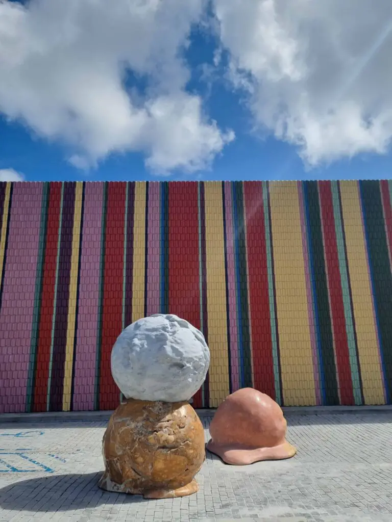Striped artwork spray painted on external walls of a building with sculptures of ice cream in front