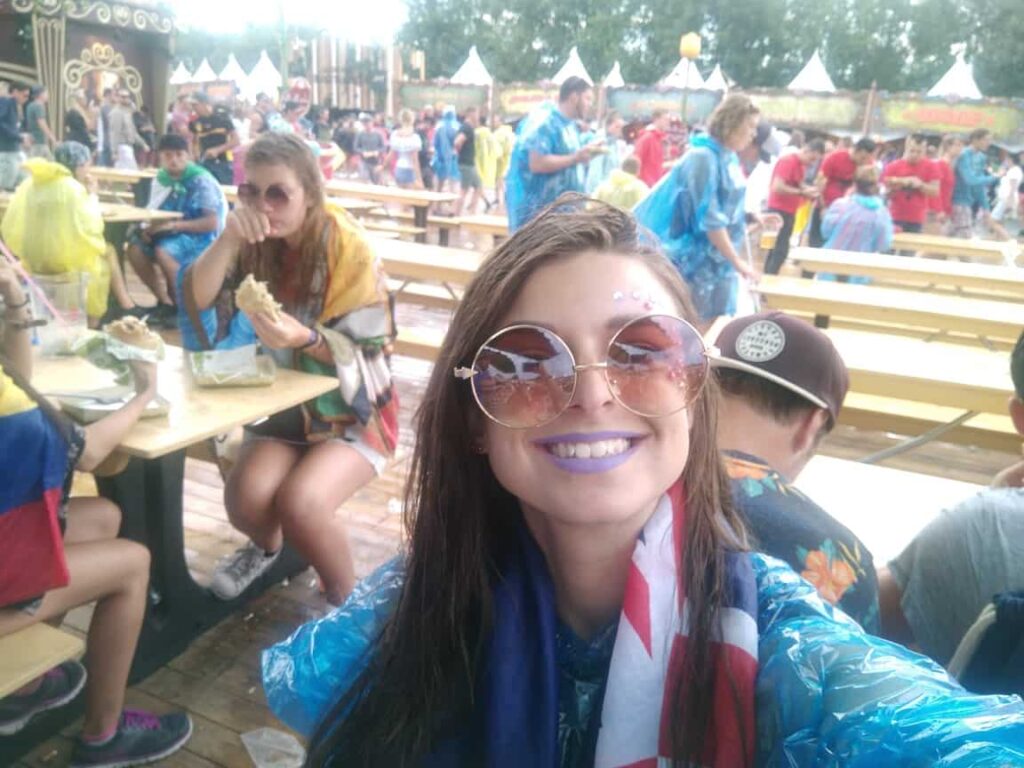 Tomorrowland Belgium: Survival Guide 2025 4 A woman smiling at the camera wearing large round glasses and wearing a New Zealand flag around her neck.