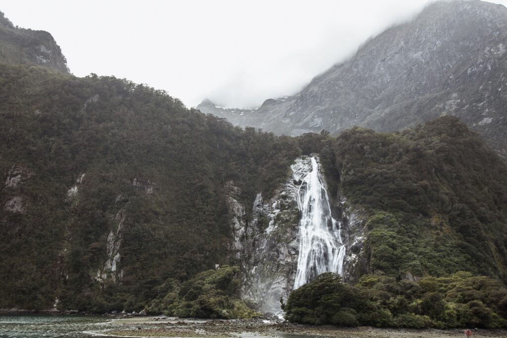 Picture of a waterfall running down a cliff face with another large mountain behind it