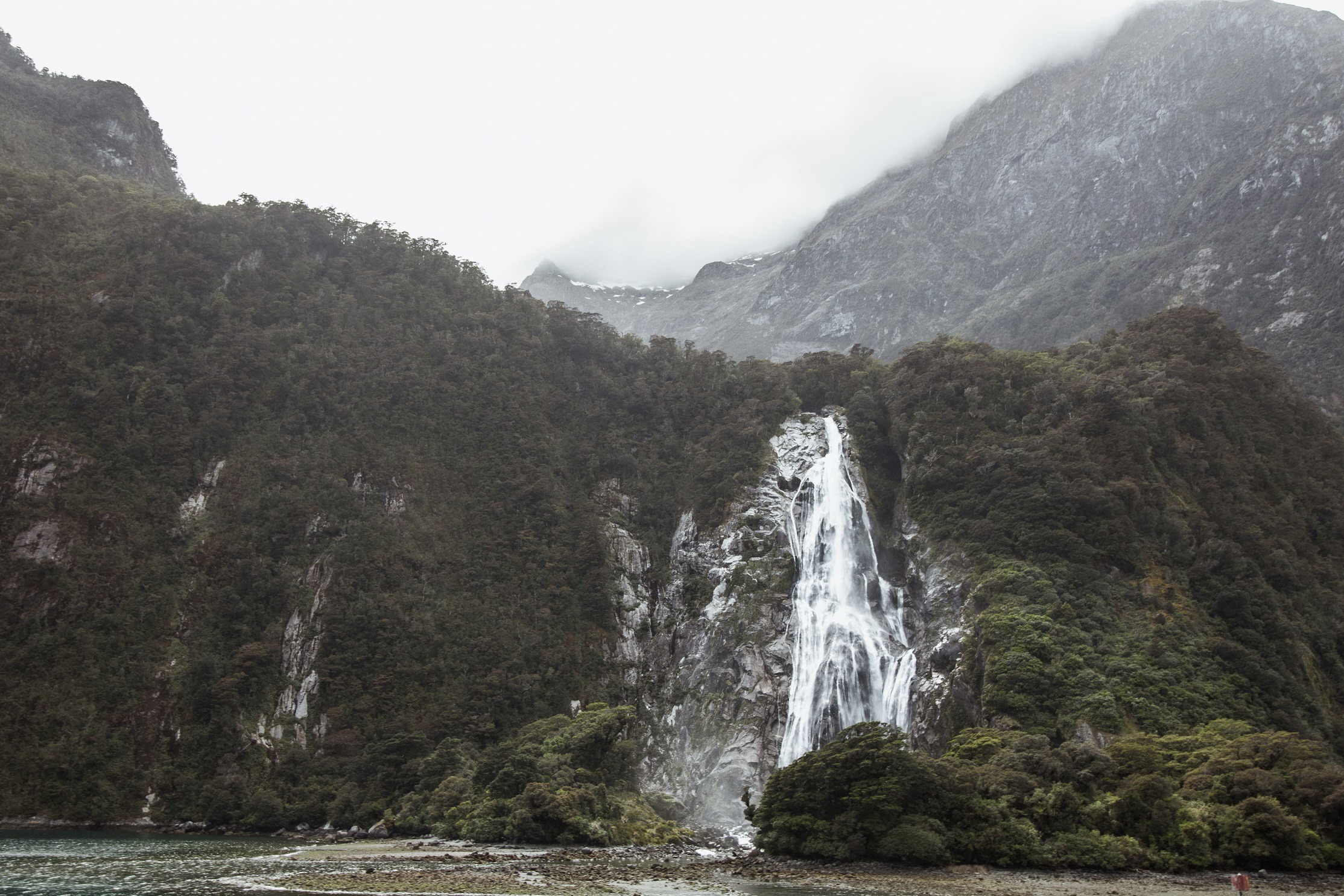 Picture of a waterfall running down a cliff face with another large mountain behind it