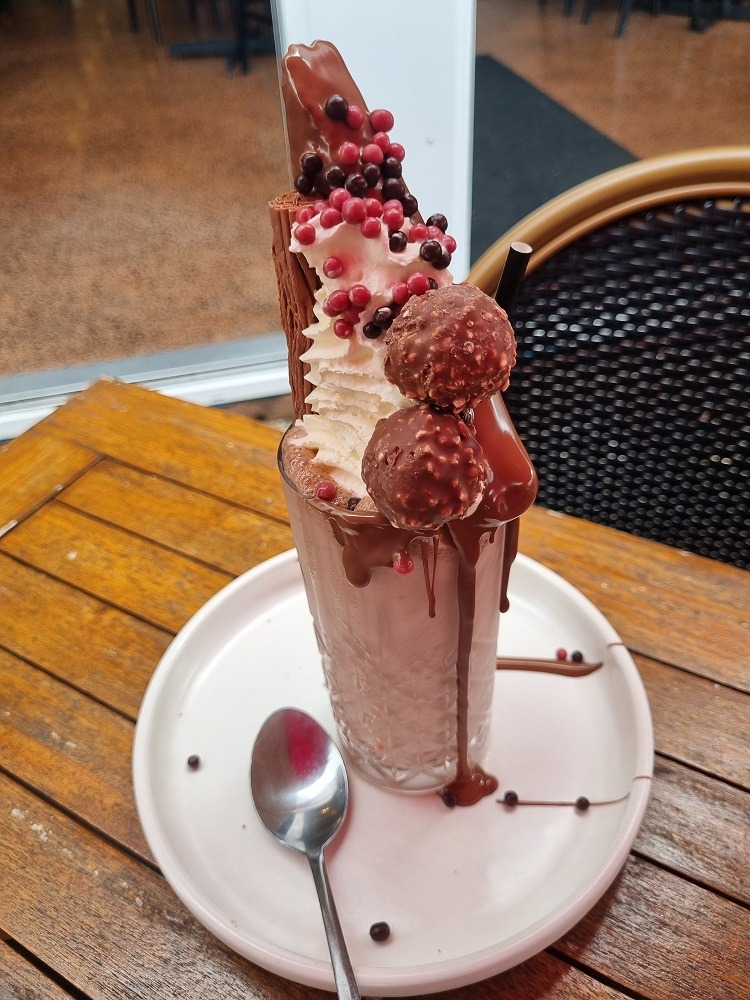 7 of The Best Indian Restaurants in Auckland 12 A picture of a large milkshake in a tall glass. This milkshake is topped with ice cream, cream, two ferrero rochers', a large brownie and a flake chocolate bar. Chocolate is dripping down the side of the glass