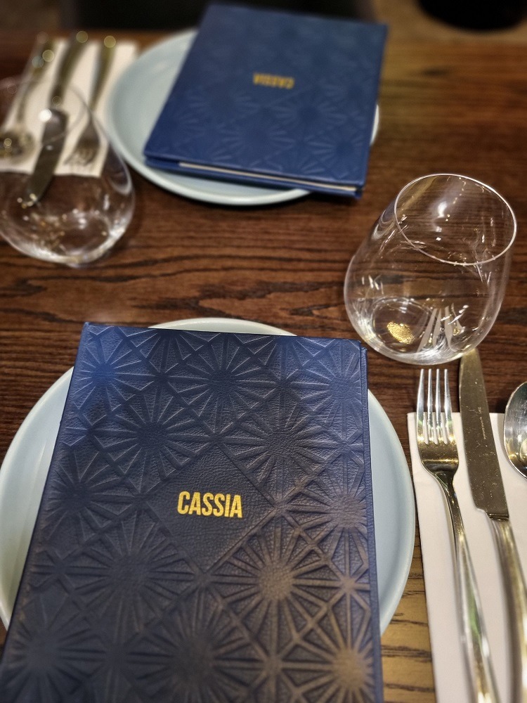 7 of The Best Indian Restaurants in Auckland 5 Two blue food menus sitting on a light blue plate with cutlery to the right side. The menu says 'Cassia', which is one of the best Indian restaurants in Auckland
