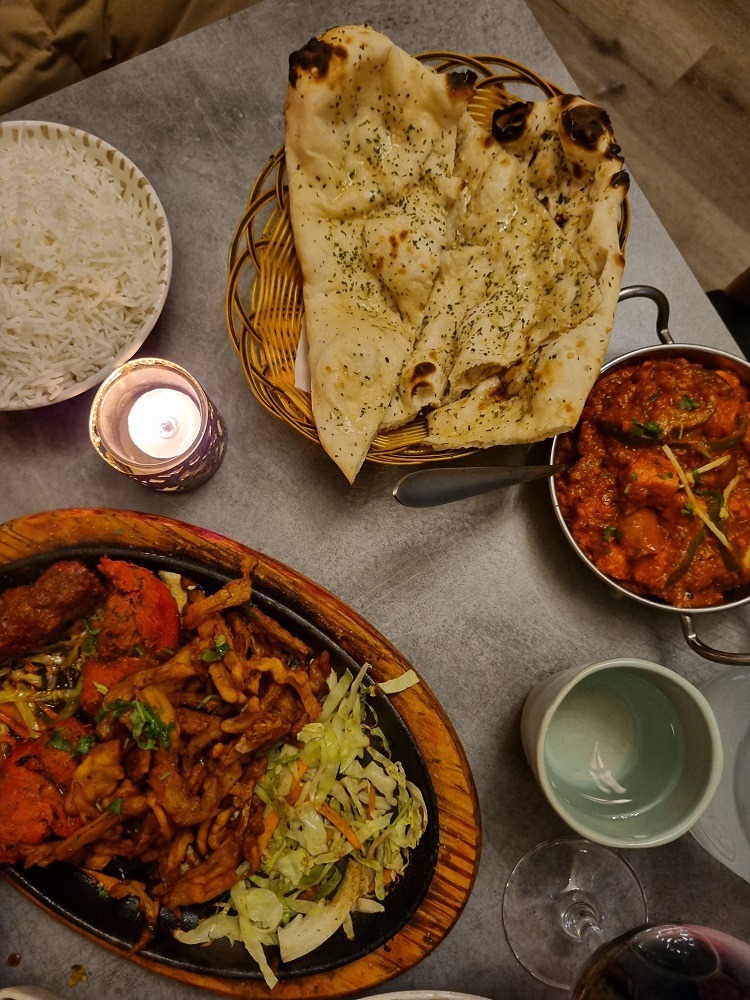 7 of The Best Indian Restaurants in Auckland 3 2 large pieces of naan bread in a basket, a red curry with large chicken pieces in a small bowl and a large hot plate with several different piece of chicken tikka, onion bhaji and vegetables, at Karam Indian restaurant in Auckland