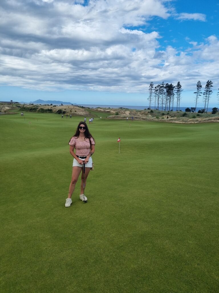 Female standing on Te Arai Links putting green. Mangawhai travel guide.