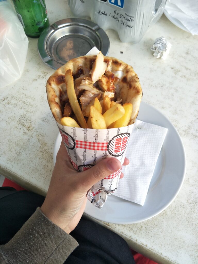 A womans hand holding a gyro whgile in Mykonos, which is a piece of flat bread containing hot chips and sauce. 