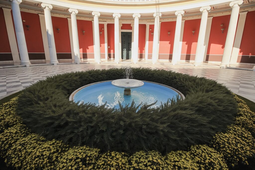 A photo of the atrium inside the Zappeion Hall in Athens. The floor is marble with black and white checkers with a water fountain in the middle.