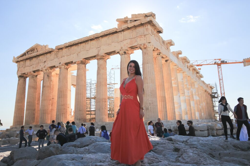 Woman wearing a long red dress standing in front of the Parthenon on the Acropolis in Athens, Greece.
