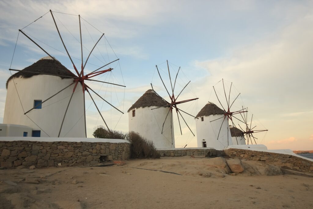 Four white windmills which sit on the waters edge in Mykonos, Greece.