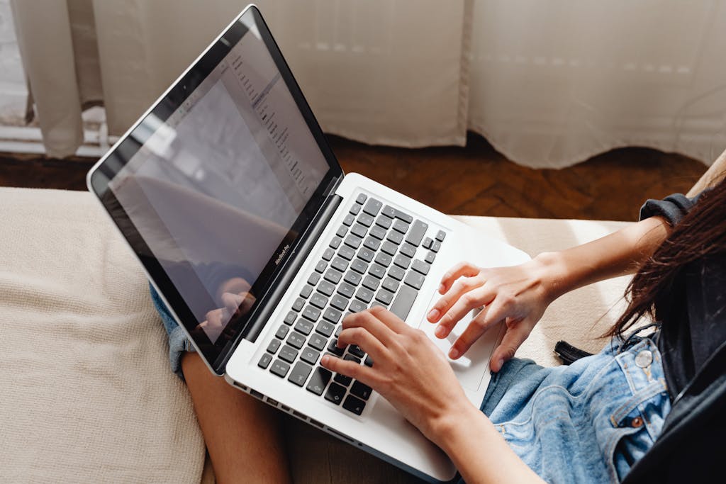Close-up of a woman's hands typing on a laptop while sitting comfortably indoors, learning how to start a blog,
