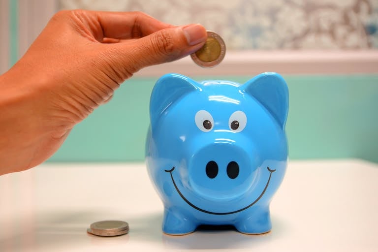 Hand inserting a coin into a blue piggy bank for making money from blogging