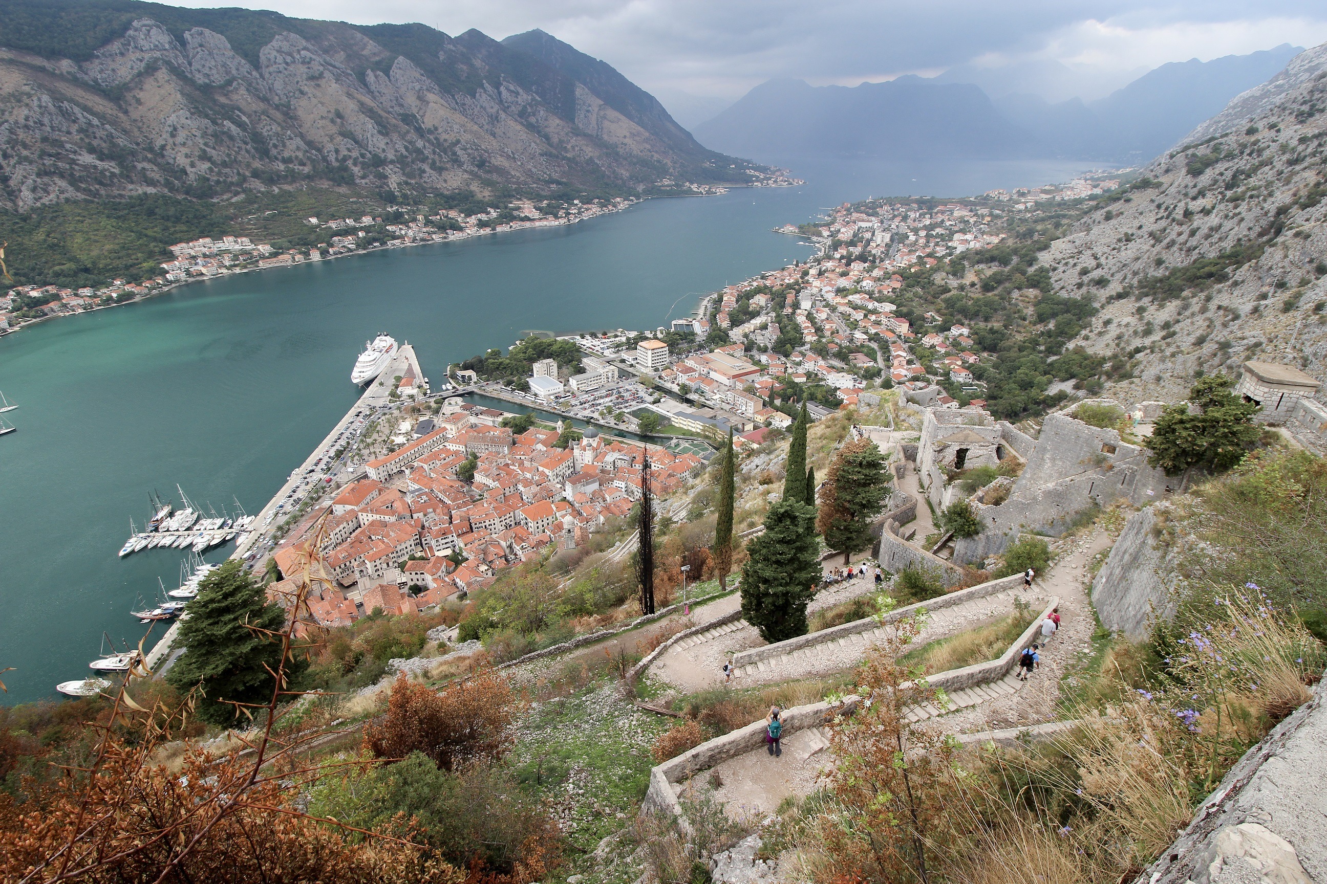 Halfway up the Ladder of Kotor showing the concrete steps trailing in a zig zag pattern back down to Kotor Old Town. Kotor Bay can be seen in the background surrounded by mountainous terrain.