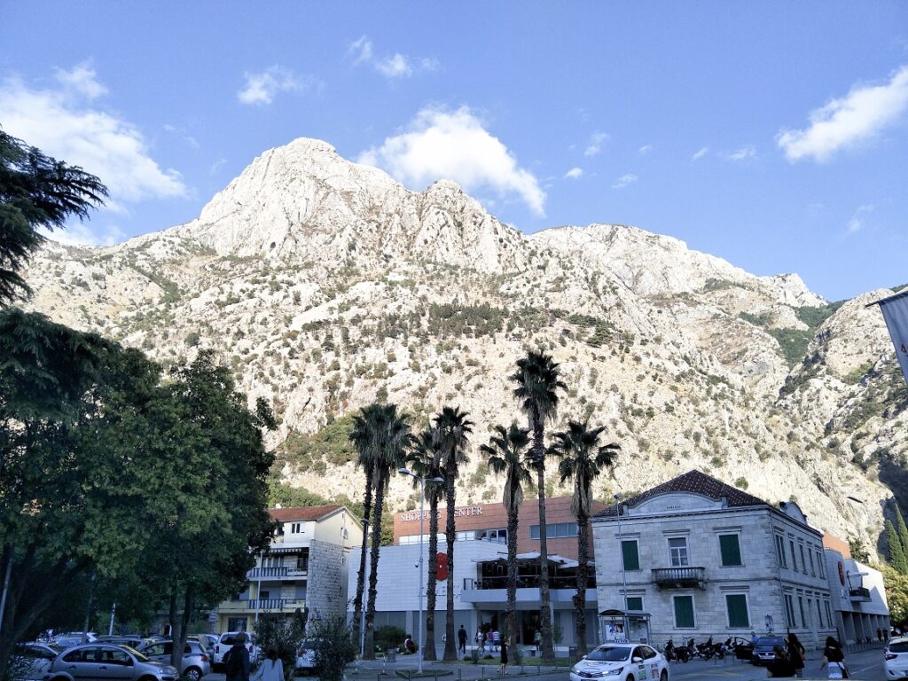 Buildings from Old Town Kotor sit in the foreground at the bottom of the image. A large mountain towering over old town is directly behind these buildings.