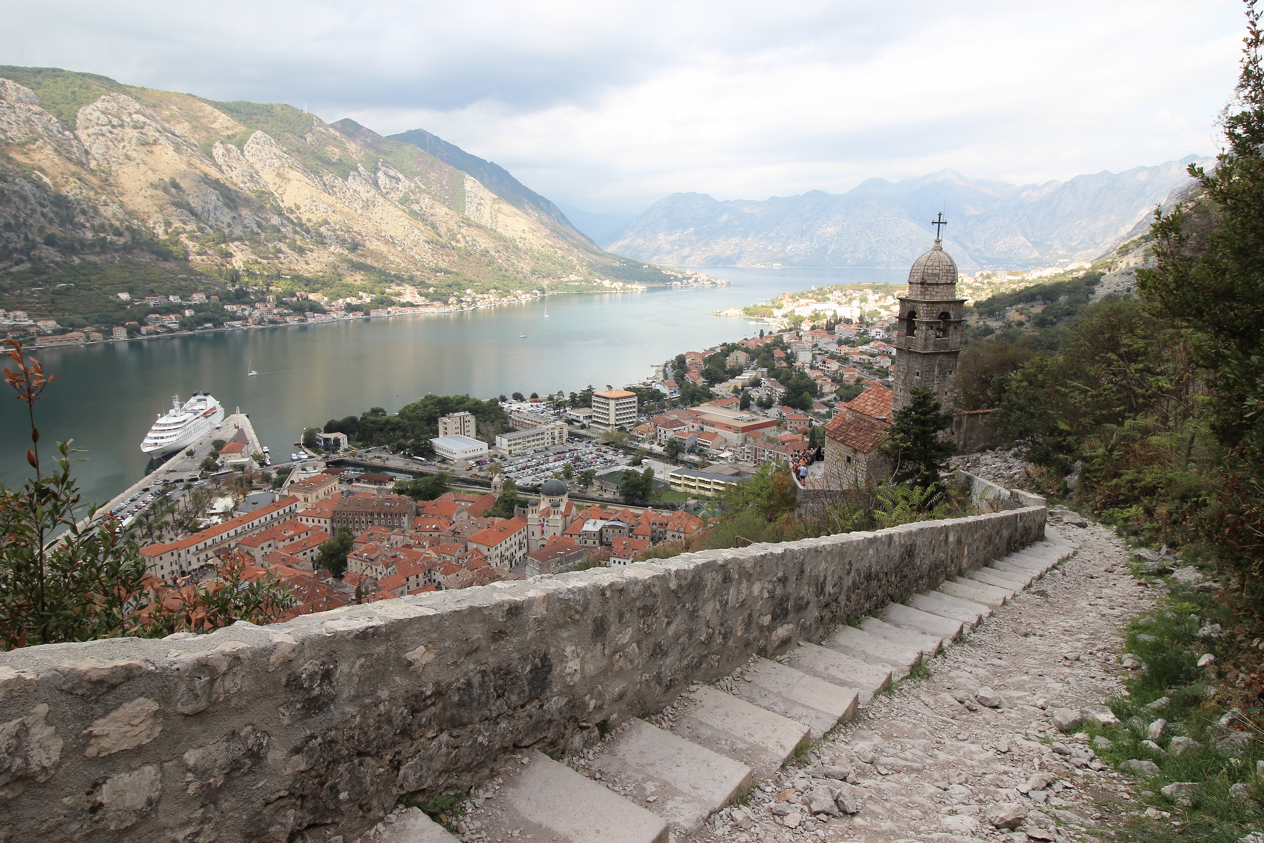 Halfway up the Ladder of Kotor showing the concrete steps trailing back down to Kotor Old Town. Kotor Bay can be seen in the background surrounded by mountainous terrain.