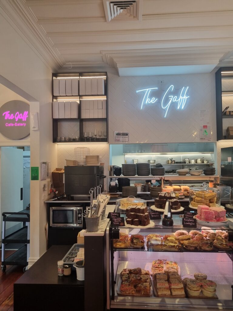 This image shows the food cabinet and counter at The Gaff in Mangere Bridge. The cabinet is full of sweat treats and savoury goods.