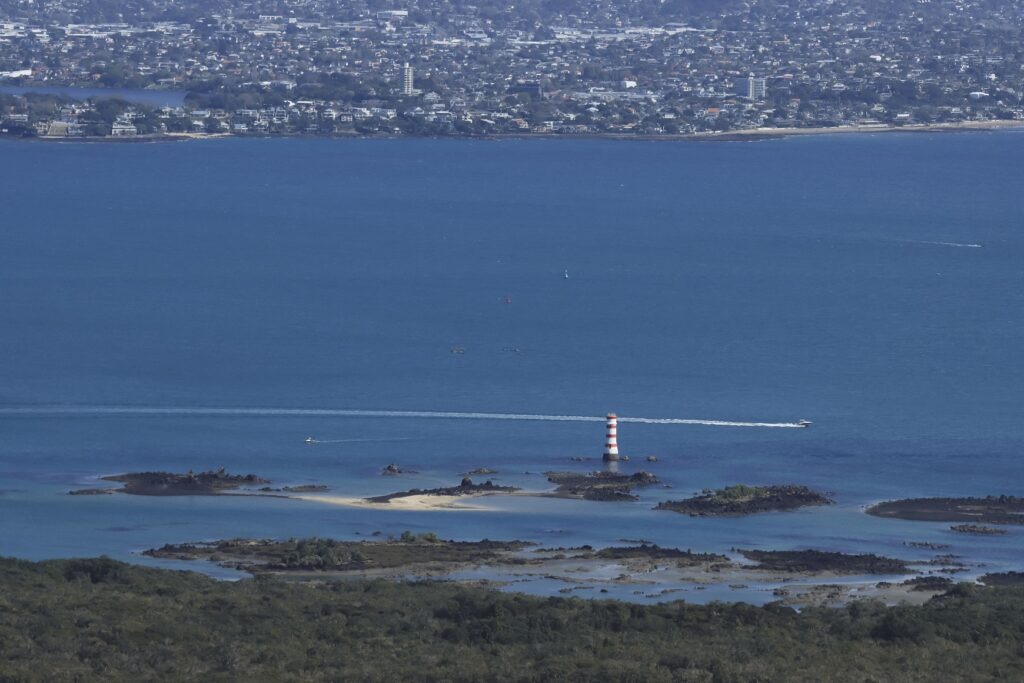 Best views from Rangitoto Island which shows a boat cruising in front of the lighthouse on the shore of Rangitoto Island