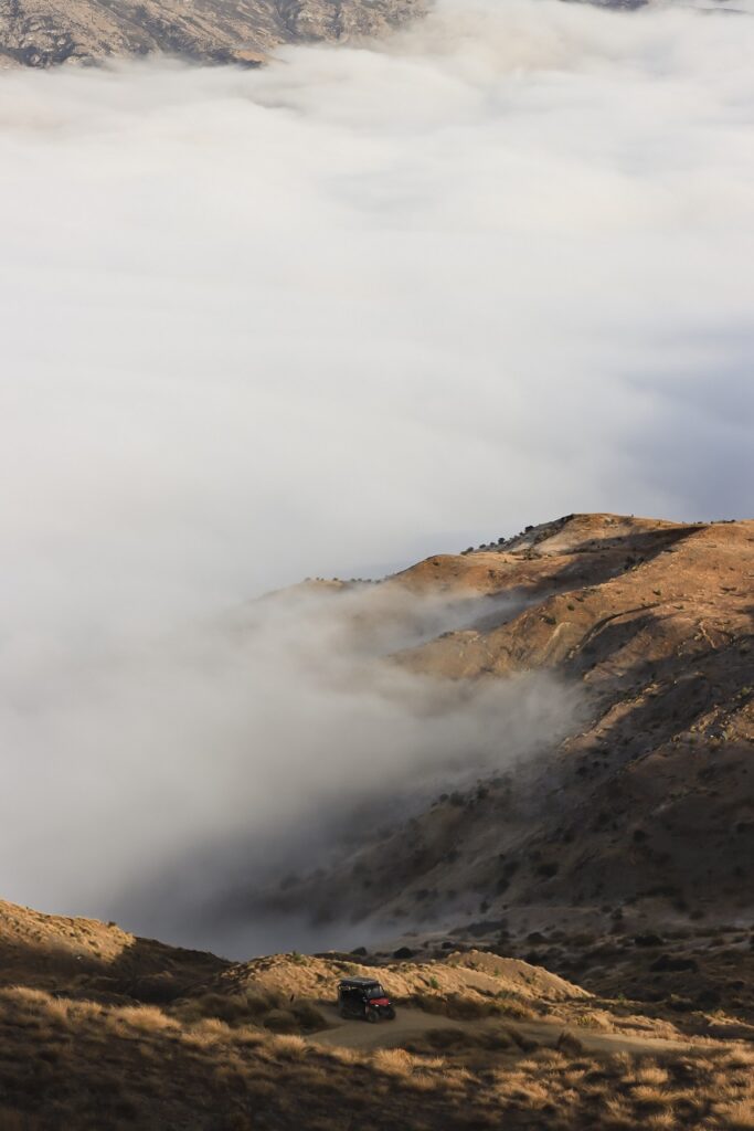 Amazing Queenstown Travel Guide 2026 Views from the top of the Crown Range in Queenstown. Thick fog is covering the lower half of the valley, sun is pouring across the grassy paddocks