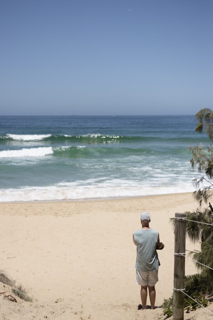 Best Beaches in Brisbane: A man is standing on white sand looking out towards the surf at a beach in Brisbane.