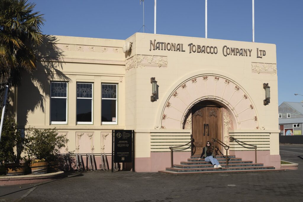 Art Deco in Napier: National Tobacco Company building. A female is sitting on the steps in front of the building smiling at the country.