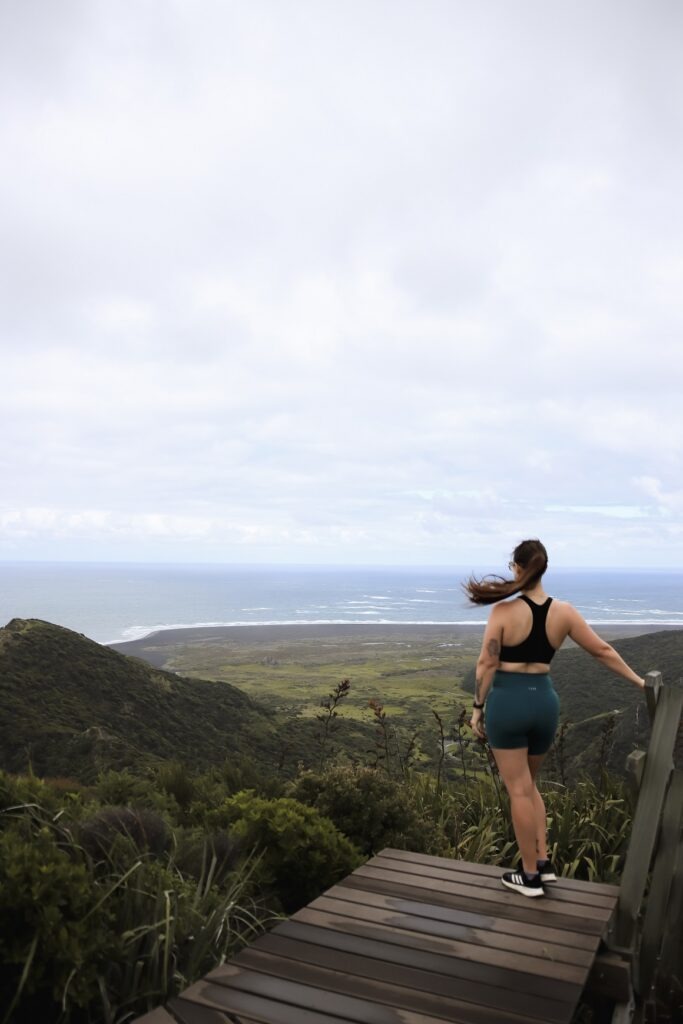Hiking Omanawanui Track: A Must-Do Auckland Hike West Auckland Hikes: Woman standing on top of a wooden staircase overlooking the ridge along Omanawanui track in Auckland